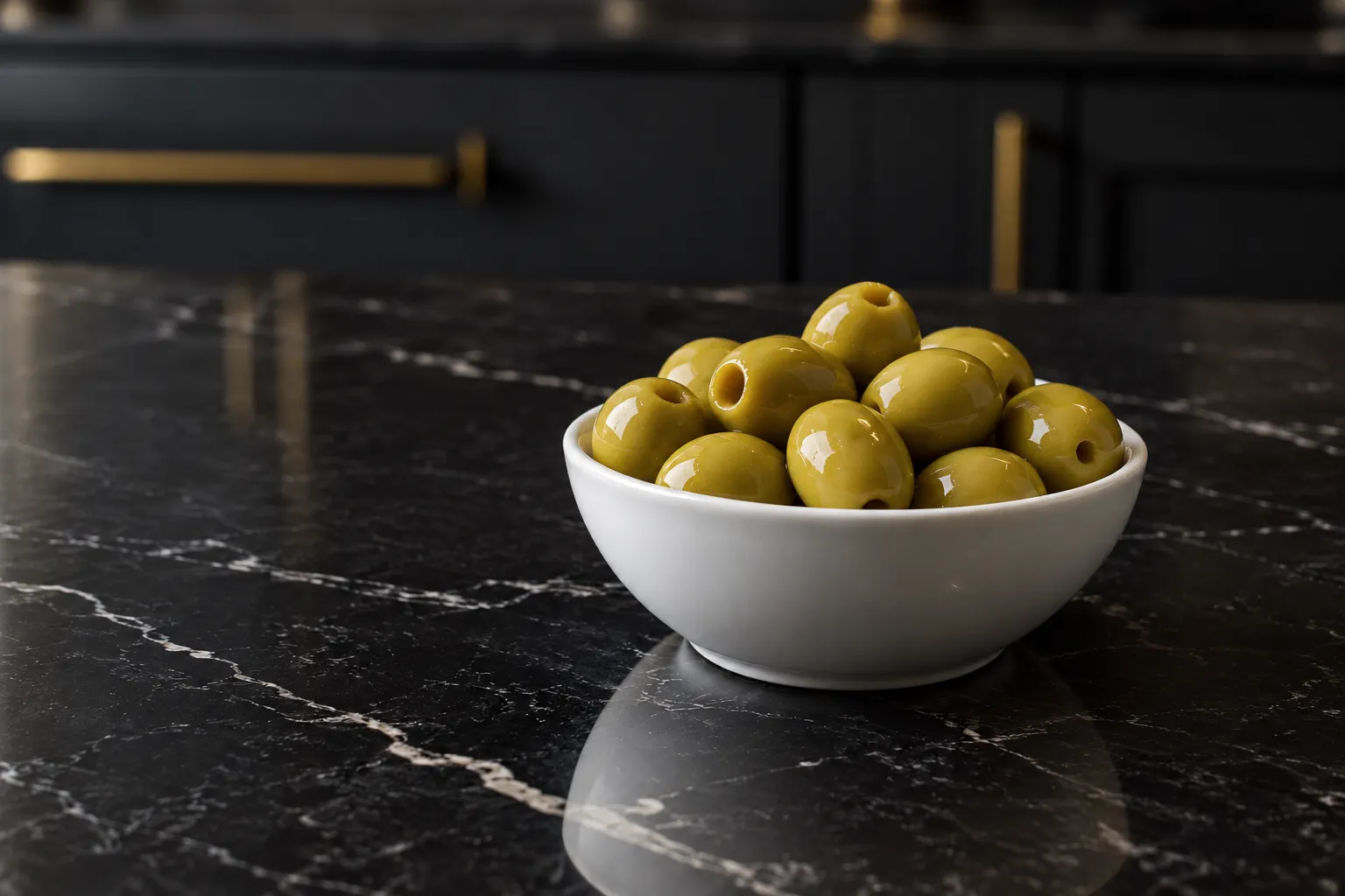 Pitted green olives in a white bowl on black marble